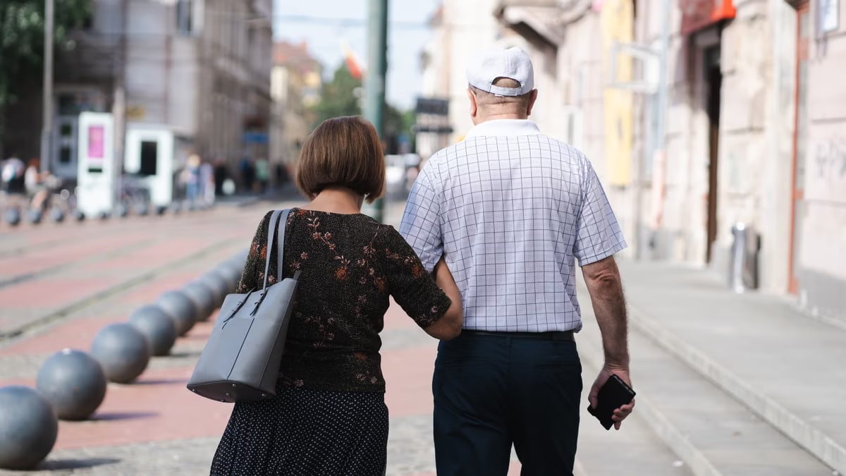 Senior couple walking arm-in-arm on a sunny urban street, capturing a moment of togetherness.